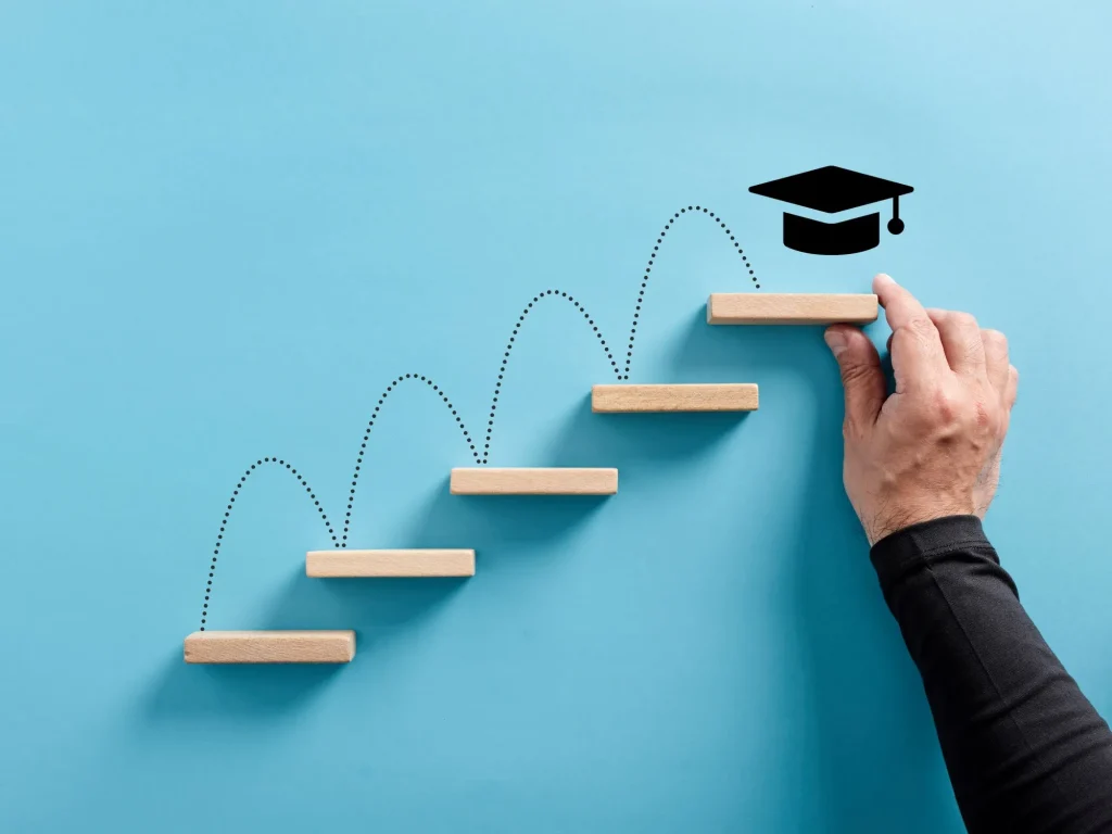 Male hand arranges a wooden block ladder with academic cap symbol. Graduation achievement and education goals.