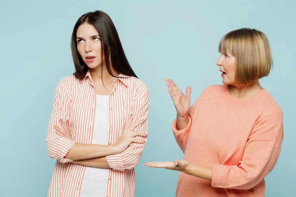 Arguing sad offended annoyed elder parent mom with young adult daughter two women together wearing casual clothes talk speak try to make up isolated on plain blue cyan background.