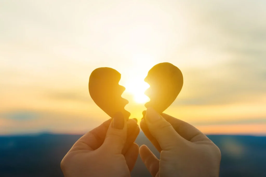 Two hands hold a broken heart on the background of the sunset. Concept spat divorce dissolution, love feelings