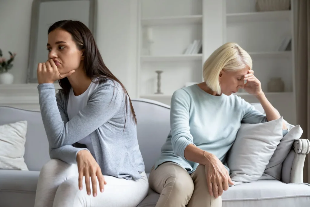 Upset mad grownup millennial girl and senior mother sit separately on couch thinking problem over after quarrel, pensive angry adult mom and daughter avoid talking after fight, family drama concept