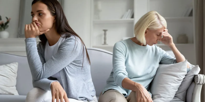 Upset mad grownup millennial girl and senior mother sit separately on couch thinking problem over after quarrel, pensive angry adult mom and daughter avoid talking after fight, family drama concept