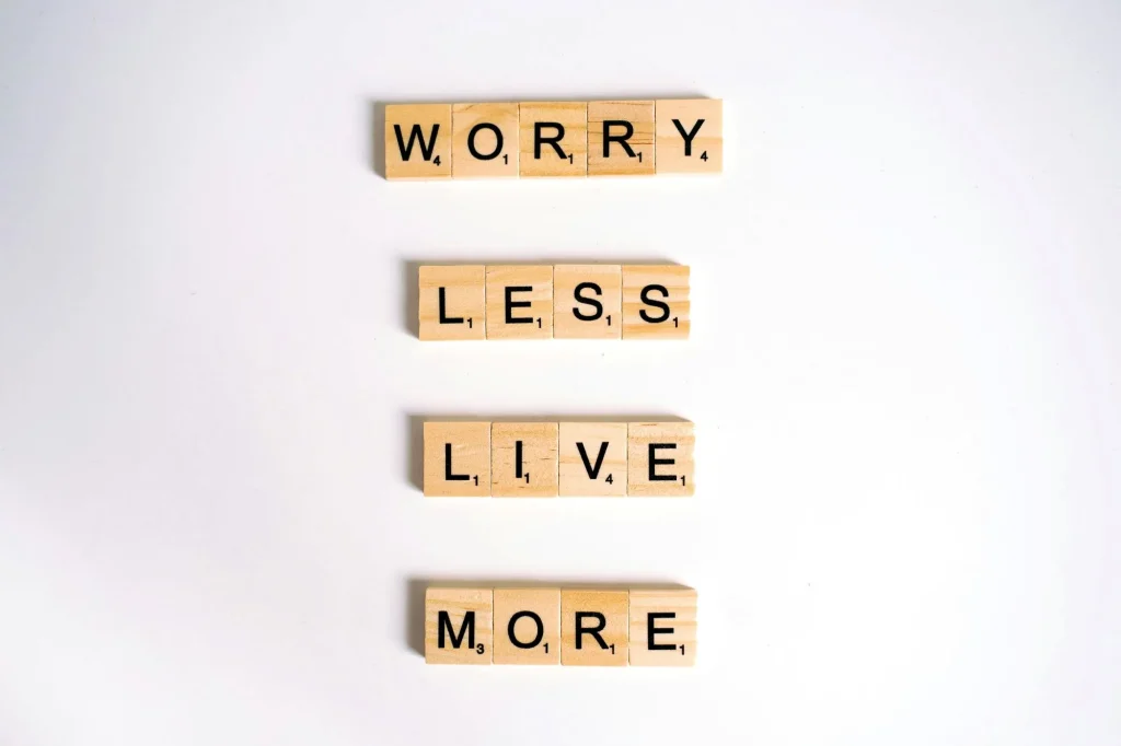 "worry less, live more" quote with scrabble tiles on white background