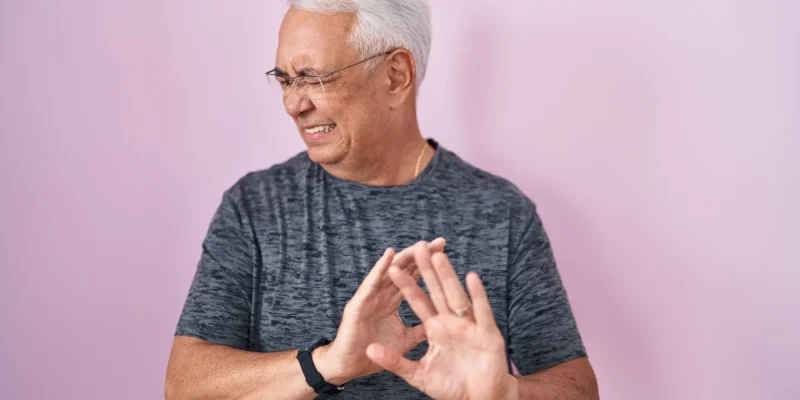 Middle age man with grey hair standing over pink background disgusted expression, displeased and fearful doing disgust face because aversion reaction