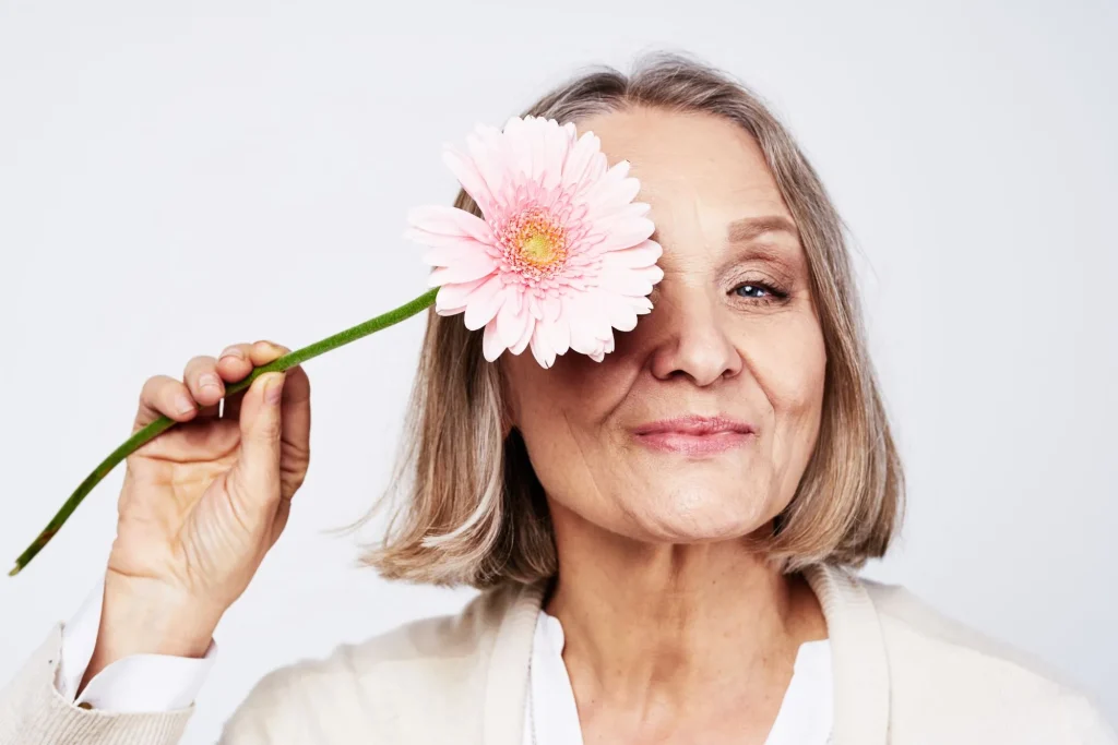 Cheerful married woman holding a flower near her face feeling confident about herself.