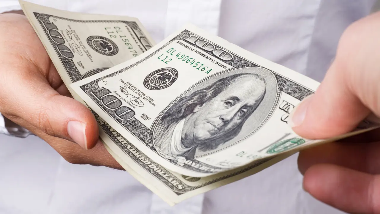 one hand handing another one-hundred dollar bills