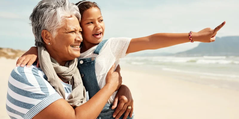grandma and granddaughter on a windy beach smiling