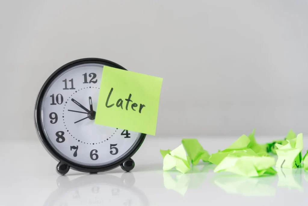 Procrastination delay and urgency concept with word later on green sticky paper over white alarm clock and crumpled paper ball, bad time management.
