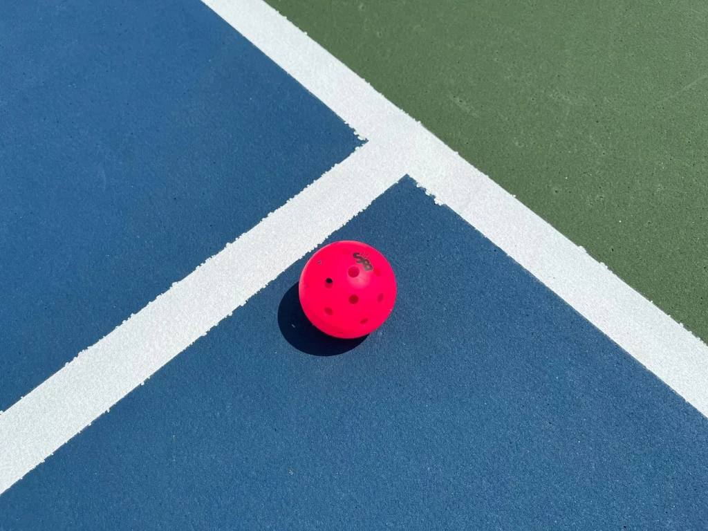 pink pickleball ball sitting on a blue court