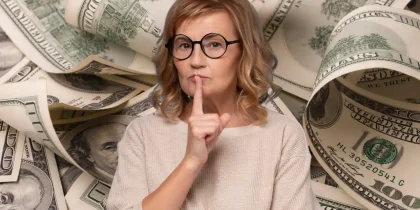 senior woman saying"shh" in front of a lot of $100 dollar bills