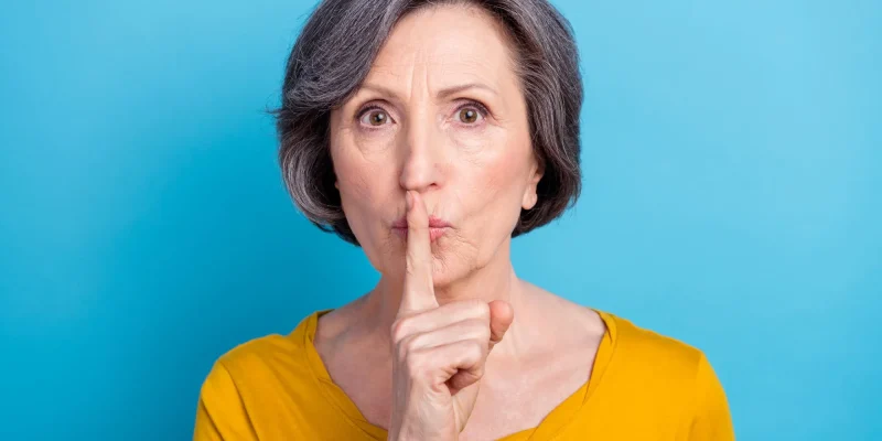 Close-up portrait of attractive mysterious middle-aged woman showing shh sign isolated over vivid blue color background