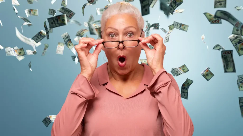 smart money senior or retiree woman with glasses down and animated look on her face on blue background with money floating