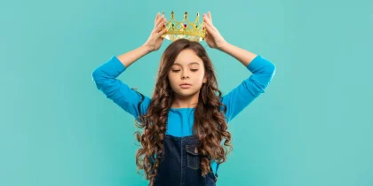 selfish kid with curly hair in princess crown on blue background, egoist, spoiled grandchild