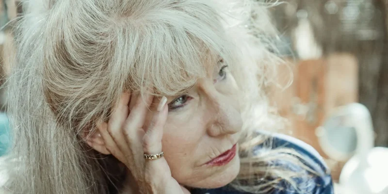 unmotivated senior woman sitting outside with head in hand