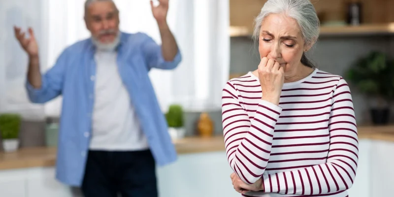 Psychological Abuse, financial abuse. Upset Senior Woman Crying In Kitchen While Arguing With Husband, Elderly Spouses Suffering Marital Crisis, Angry Man Standing On Background And Blaming Wife, Selective Focus