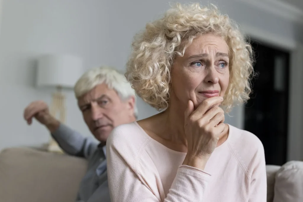 Close up shot of sad disappointed unhappy older woman suffers from misunderstanding or resentment sit on sofa with frown angry husband after quarrel. Break up, divorce, emotional abuse, bad relations