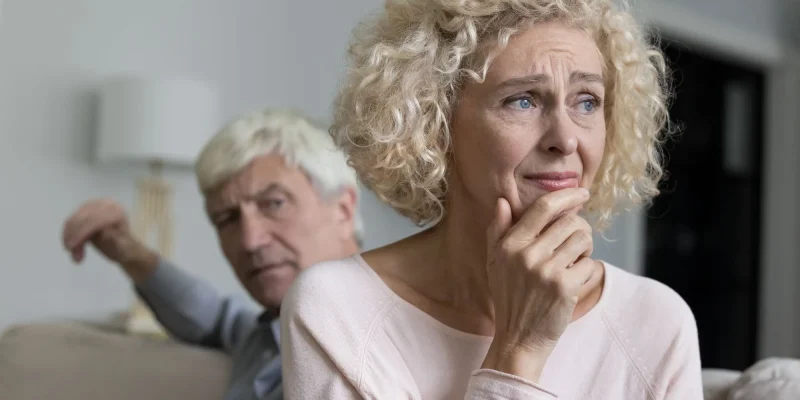 Close up shot of sad disappointed unhappy older woman suffers from misunderstanding or resentment sit on sofa with frown angry husband after quarrel. Break up, divorce, emotional abuse, bad relations