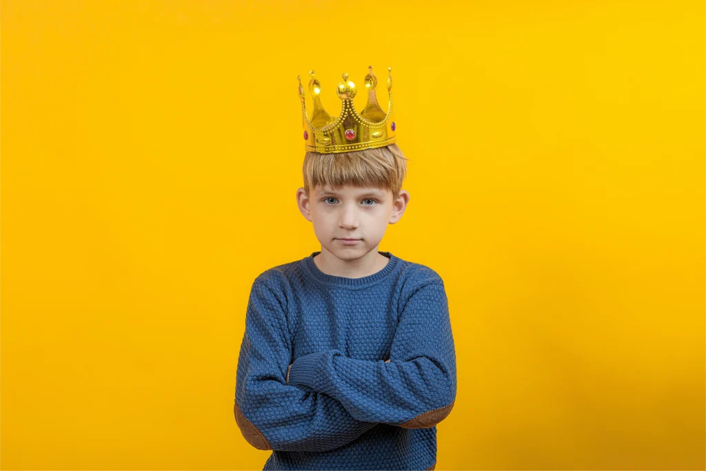 young boy wearing a crown, blue shirt, yellow background