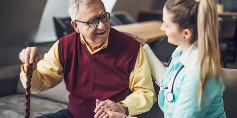 Nurse home caregiver is assisting old man at his home. Professional health support for elderly people.