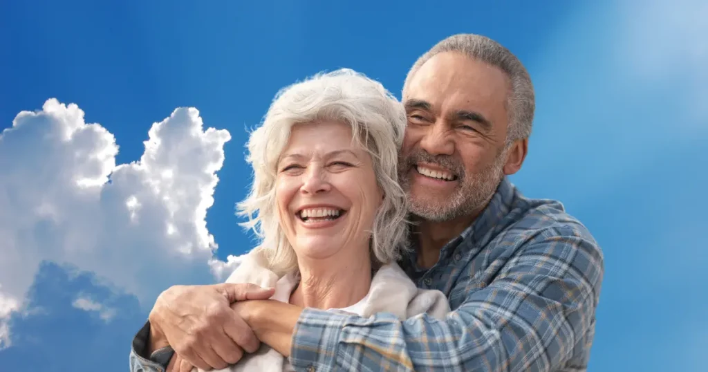 senior retiree couple smiling in front of a blue sky with clouds