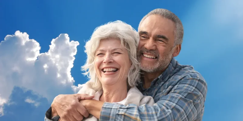 senior retiree couple smiling in front of a blue sky with clouds