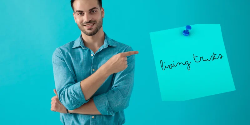 young guy on a blue background pointing to a sticky note that says living trusts