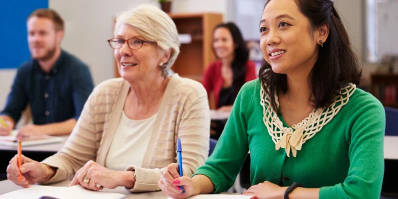 Two women sharing a desk at an adult education class look up
