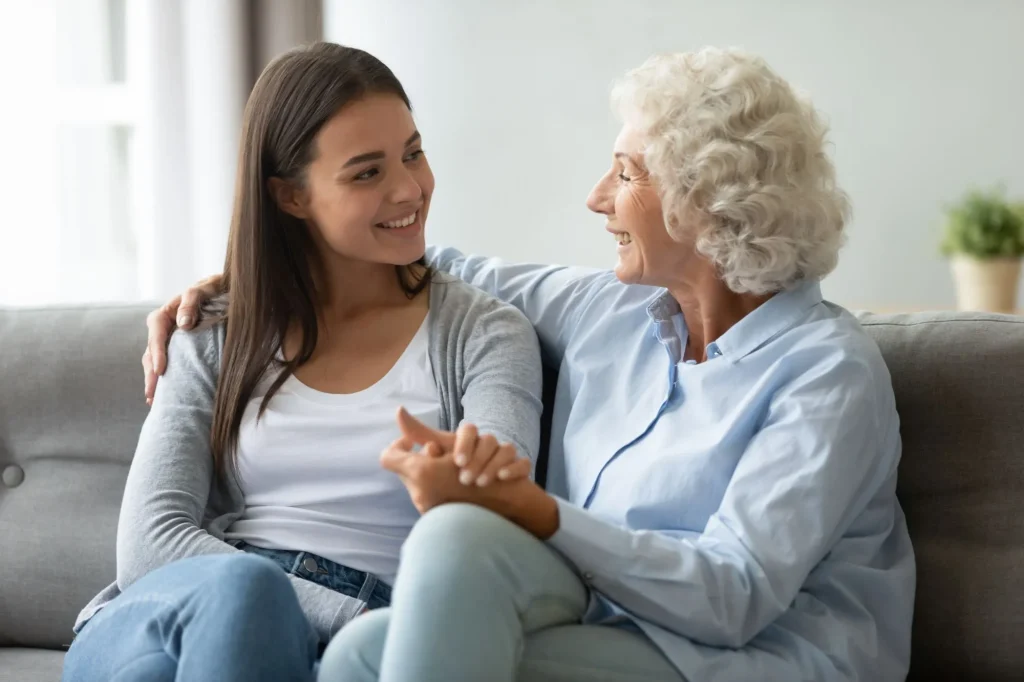 Old senior mother and young adult daughter talking bonding sit on sofa, smiling elder grandma embracing grown granddaughter having trust conversation, two age generation women family chatting at home