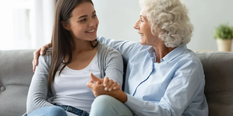 Old senior mother and young adult daughter talking bonding sit on sofa, smiling elder grandma embracing grown granddaughter having trust conversation, two age generation women family chatting at home