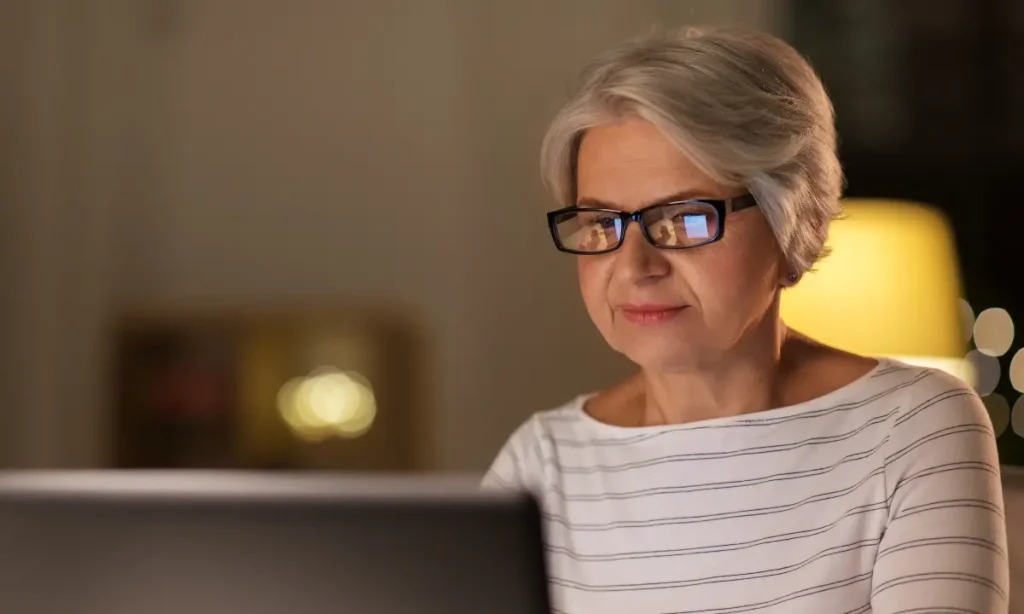 senior woman using a computer in the vening, monitor reflection in her glasses