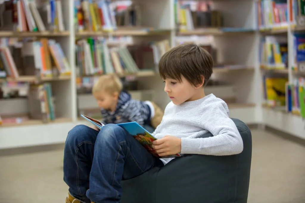 Smart children, boy brothers, toddler and school kid, educating themselves in a library, reading books and looking at pictures