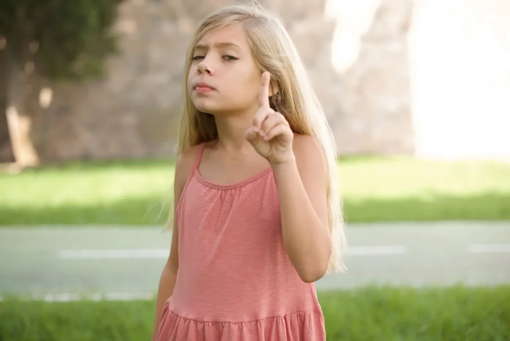 No sign gesture. Closeup portrait unhappy beautiful Caucasian little kid girl wearing dress standing outdoors raising fore finger up saying no. Negative emotions facial expressions, feelings