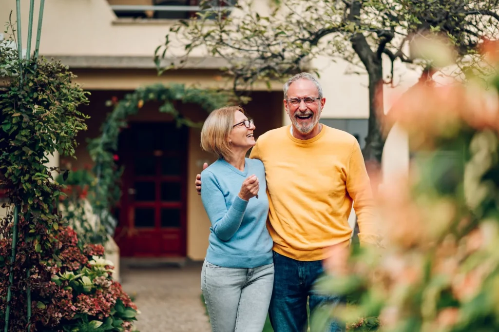 Portrait of a senior married couple holding keys and standing outside their new home on a moving day and hugging. Mature people outside their new house.