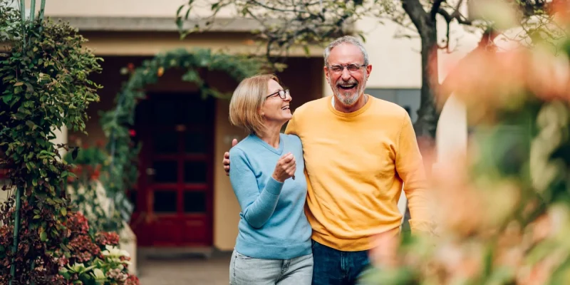 Portrait of a senior married couple holding keys and standing outside their new home on a moving day and hugging. Mature people outside their new house.