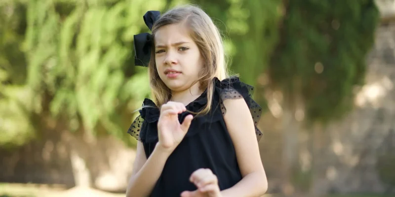 Displeased little girl standing outdoors dressed casual, says fie and has dissatisfied facial expression