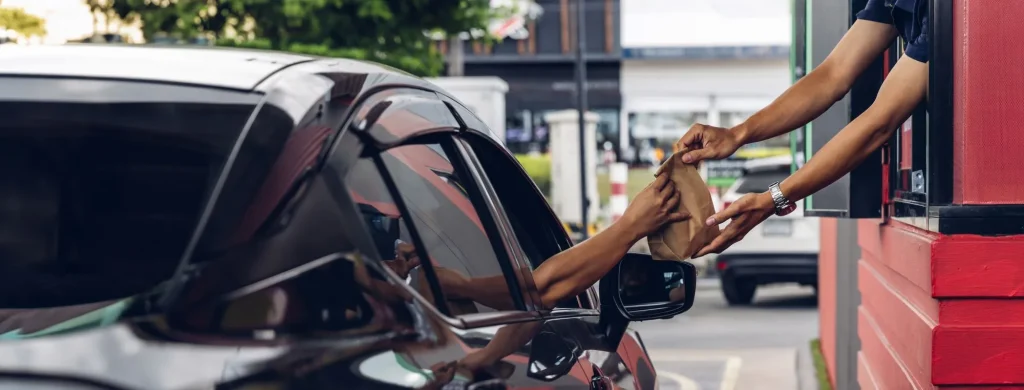 car with hands receiving a bag from a fast food drive thru window