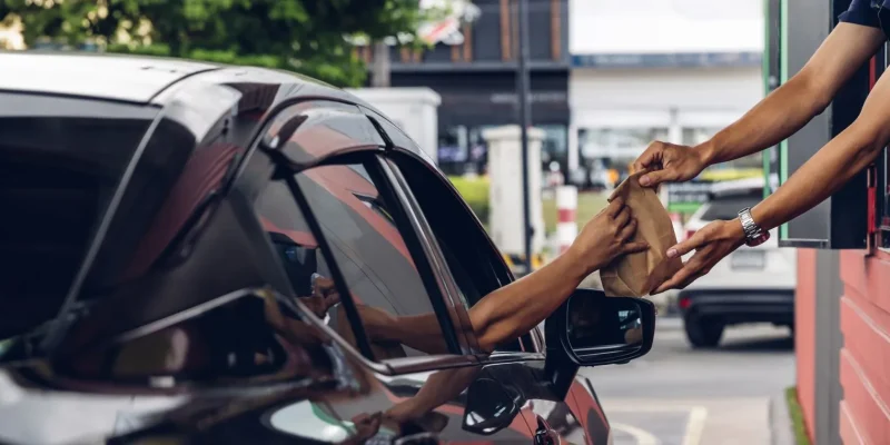 car with hands receiving a bag from a fast food drive thru window