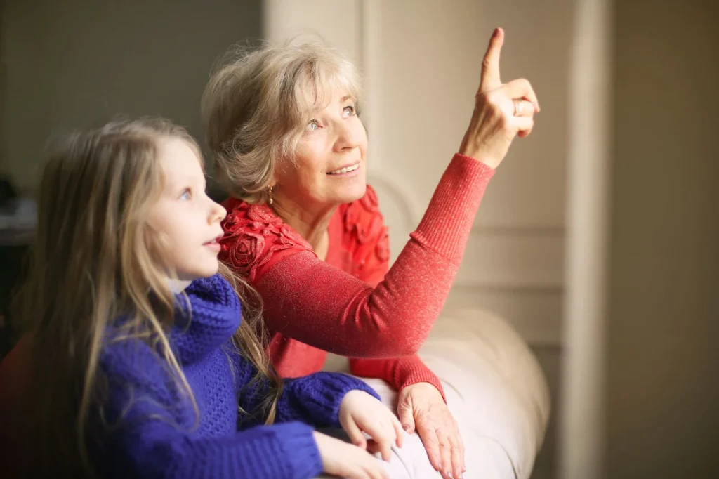 grandmother sitting by window with granddaughter pointing up and smiling