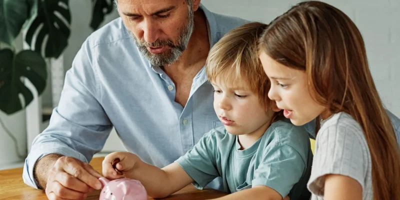 grandfather helping grandchildren learn saving and investing with a piggy bank