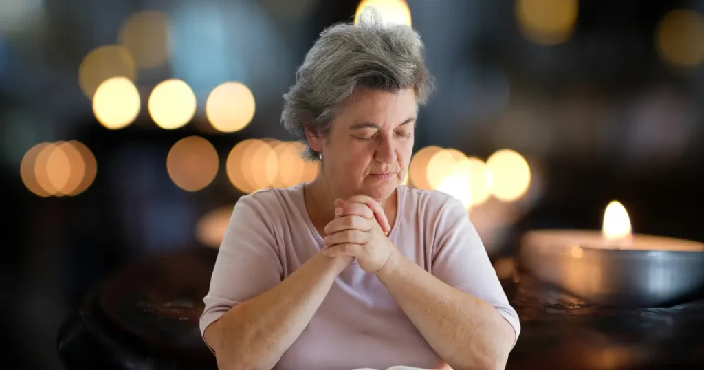 senior woman with eyes closed and praying near candles