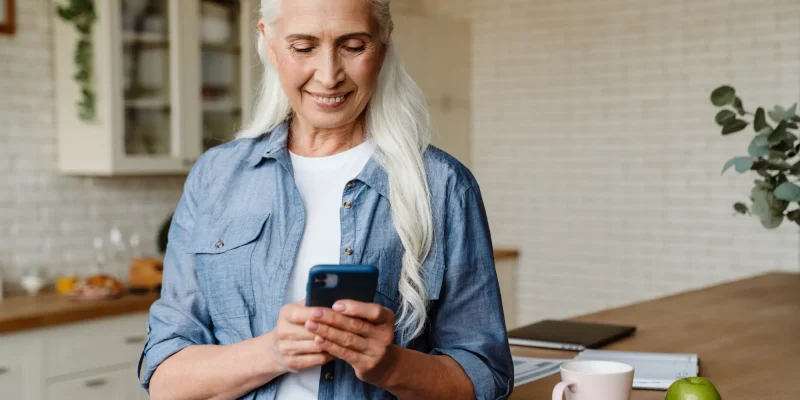 senior woman with long gray hair smiling and dialing a phone