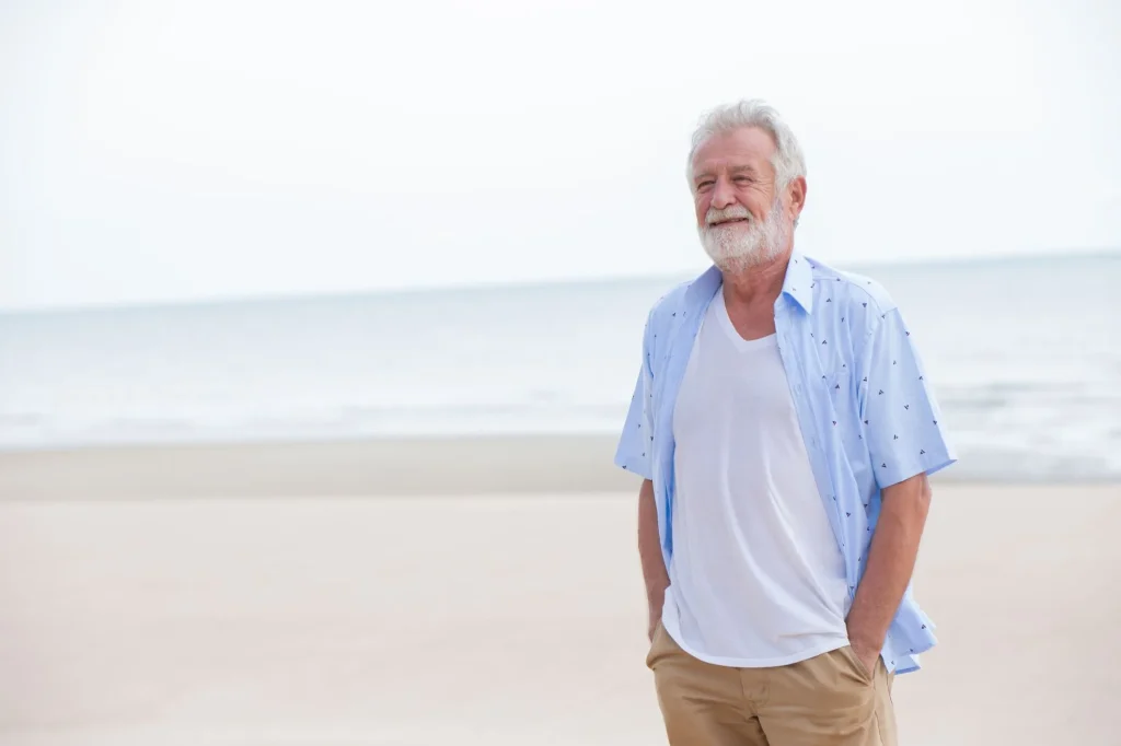 older senior man standing on the beach smiling, looking fulfilled, satisfied, content, happy