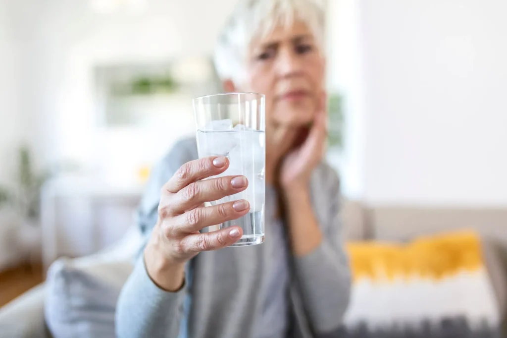 senior woman holding a glass of water, water in focus, woman out of focus, looking unsure