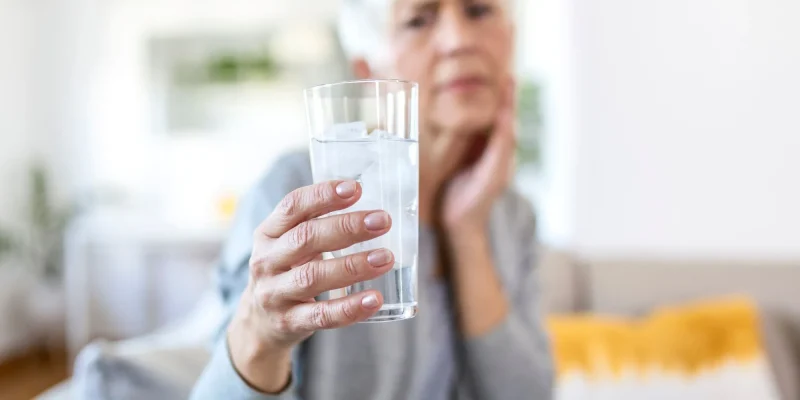 senior woman holding a glass of water, water in focus, woman out of focus, looking unsure