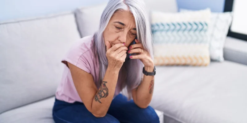 Middle age grey-haired woman talking on smartphone with worried expression at home