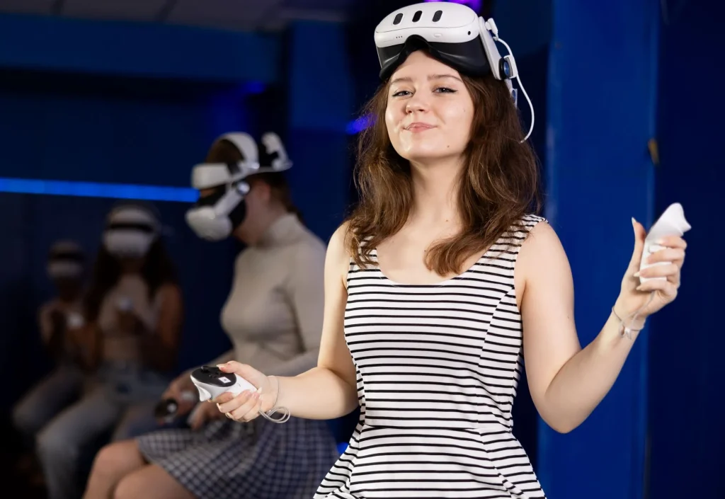 Cheerful teen girl with VR headset and controllers, eagerly anticipating virtual reality experience during fun-filled get-together with friends in modern gaming lounge
