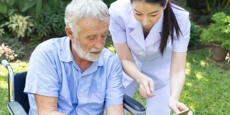 senior man in wheelchair outside looking at a care plan with an aide in an assisted living or nursing care facility
