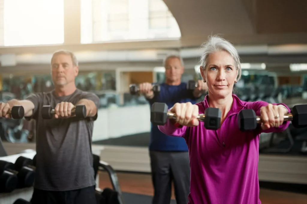 Fitness, training and senior people with dumbbells at gym for club exercise, wellness or cardio, health or strength. Class, workout or elderly friends at sports studio for bodybuilding weightlifting