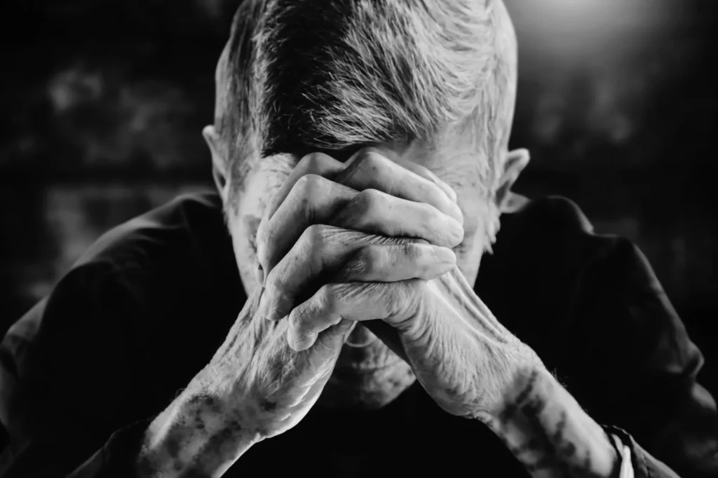 Black and white photo of a man with hands together pressed against forehead during a dramatic moment of prayer.