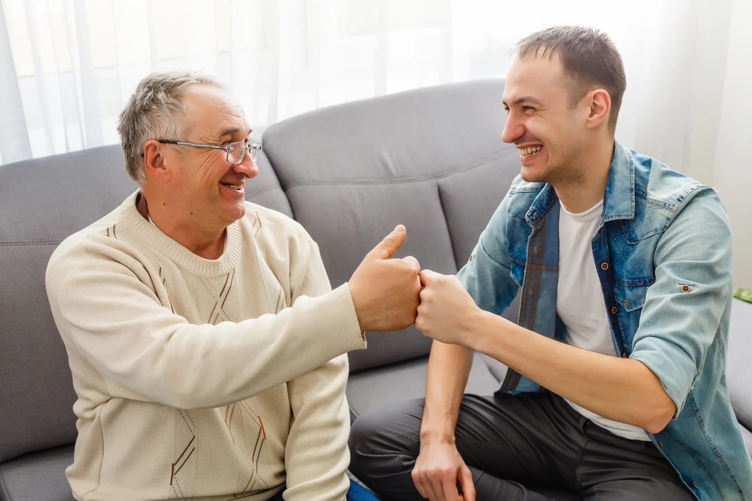 senior man and college student man sitting on living room couch smiling and doing a fist bump