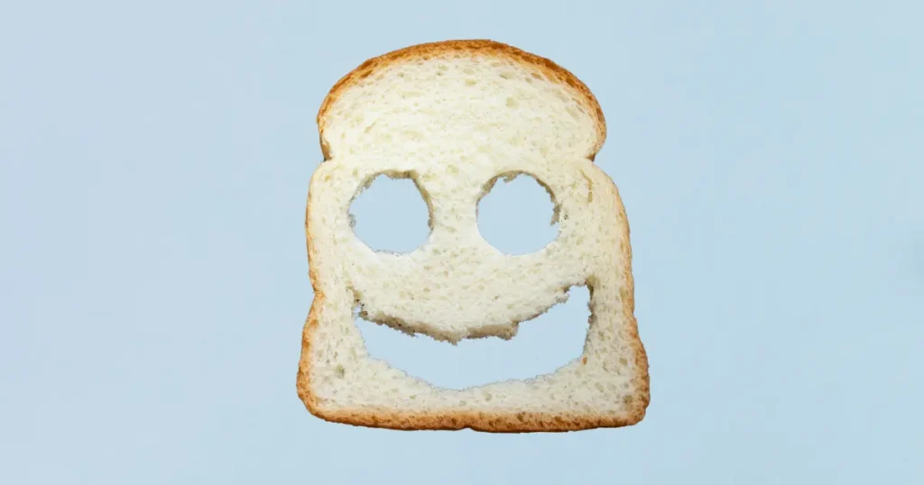 a piece of bread with two eyes and a happy face punched out on a light blue background